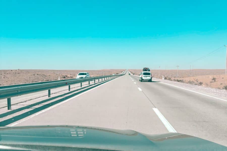 driving on the bukhara to khiva highway through the uzbek desert, a straight open road with sparse traffic and wide barren landscape under a clear blue sky