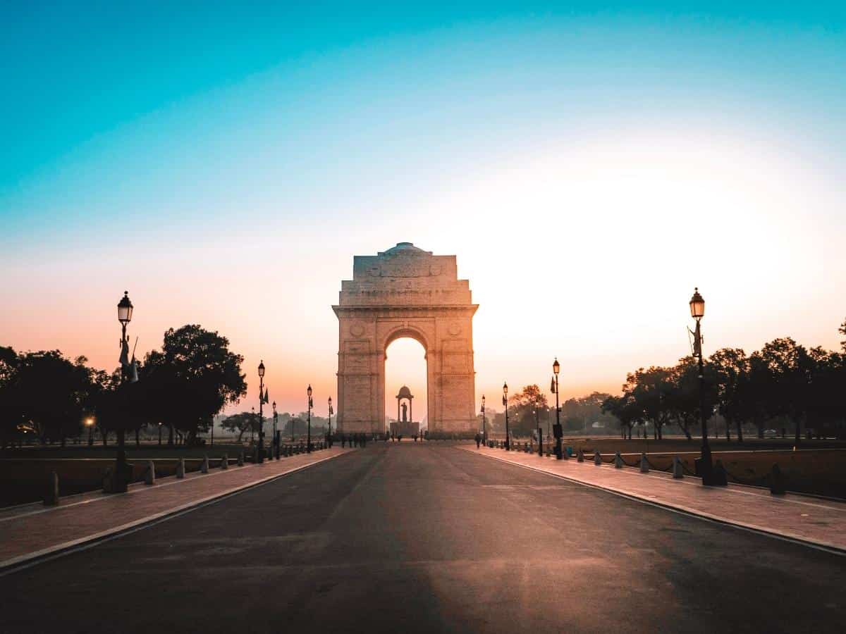 india gate glowing at sunrise, standing tall at the end of kartavya path in new delhi with warm morning light, empty road and soft gradient sky adding to the serene early hour scene