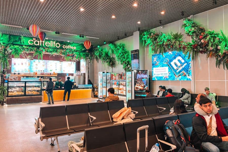 clean and modern airport lounge or waiting area in tashkent uzbekistan with clean seating, a café counter, packaged food displays, and travelers sitting comfortably under bright lighting