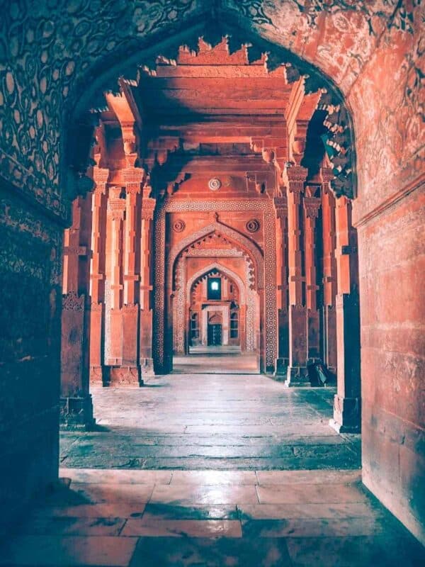 symmetrical red sandstone hallway inside jama masjid at fatehpur sikri, with intricate mughal architecture and repeating archways
