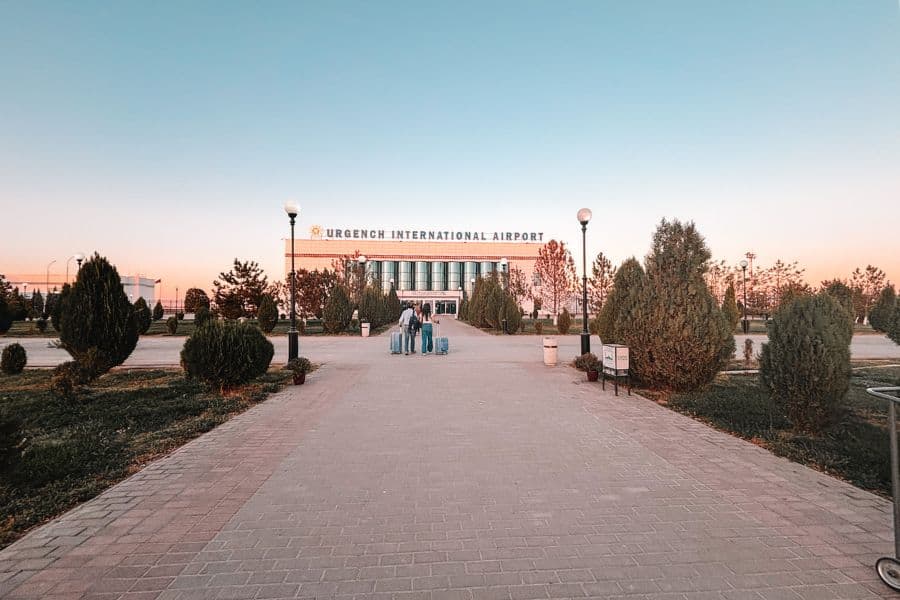entrance walkway of urgench international airport in uzbekistan, with hubby and mini-me pulling suitcases toward the terminal building