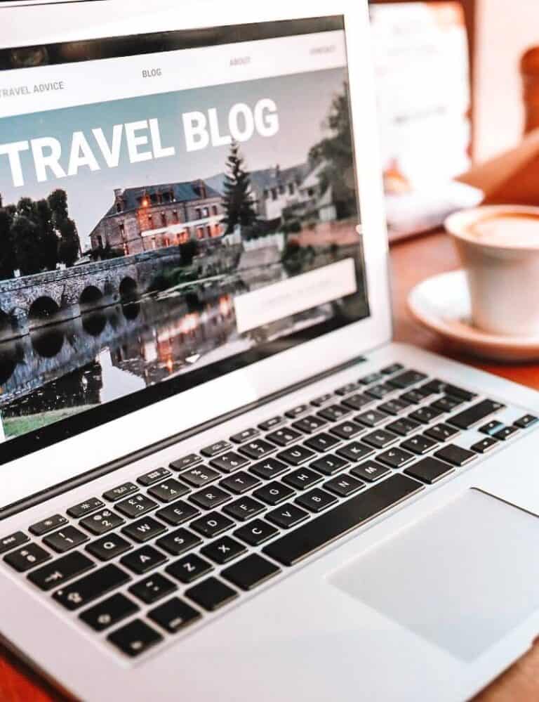 laptop showing a travel blog with a cup of coffee on its side