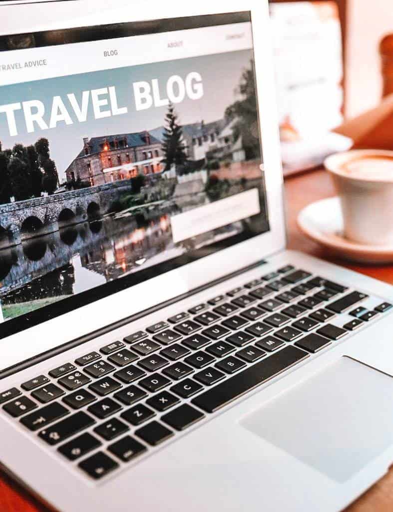 laptop showing a travel blog with a cup of coffee on its side