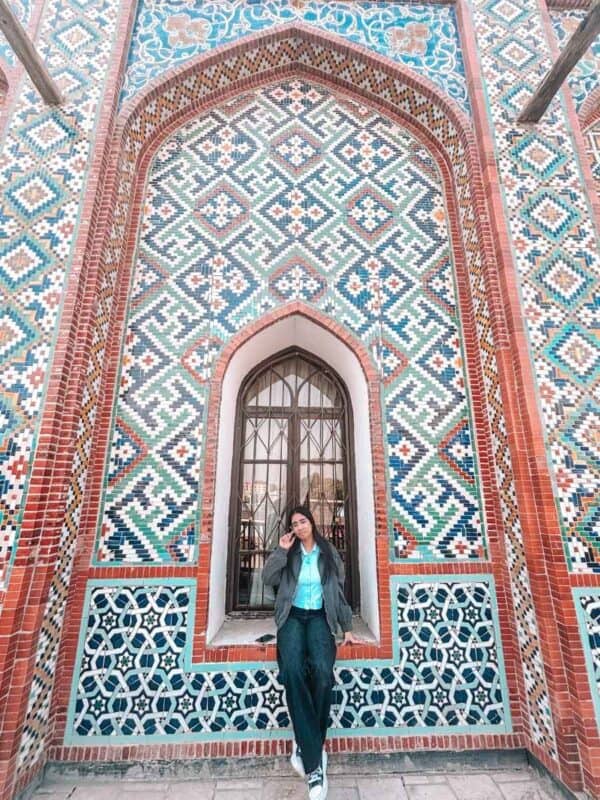 my teen girl posing by a colourful tiled wall at khudayar khan palace in kokand