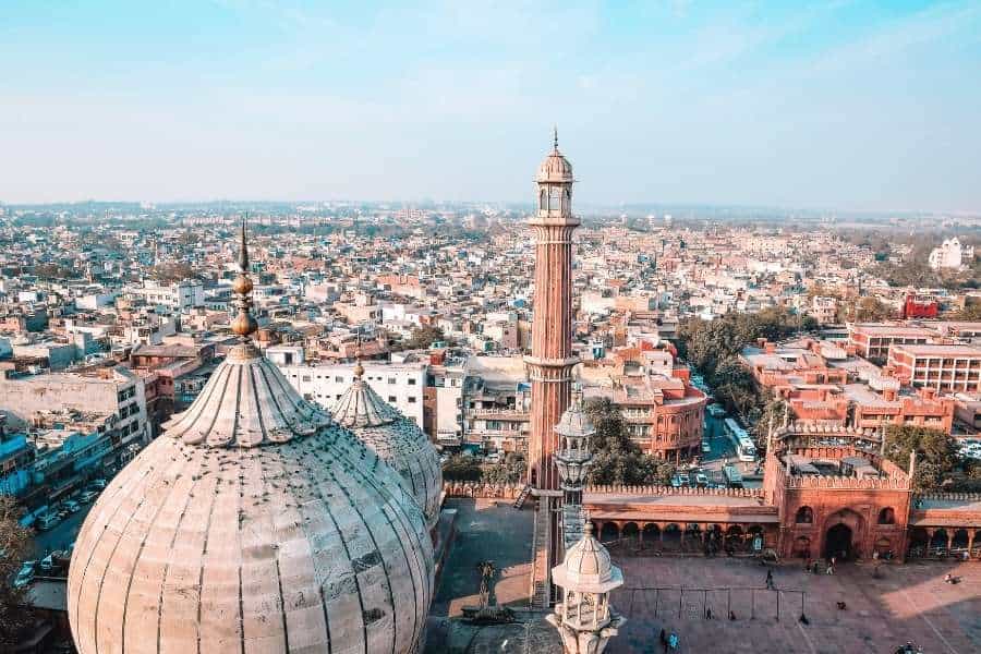 aerial view of jama masjid in old delhi with its domes and minarets in the foreground, surrounded by a sprawling cityscape under a clear blue sky