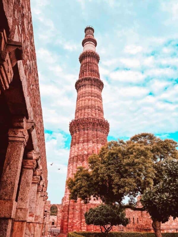 qutub minar rising behind ancient stone arches and green trees under a blue sky