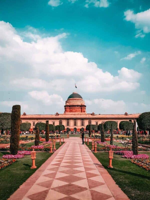 people walking through the colorful gardens of rashtrapati bhavan in spring, surrounded by manicured lawns and vibrant seasonal flowers, under a bright sky in new delhi during the annual udyan utsav flower festival