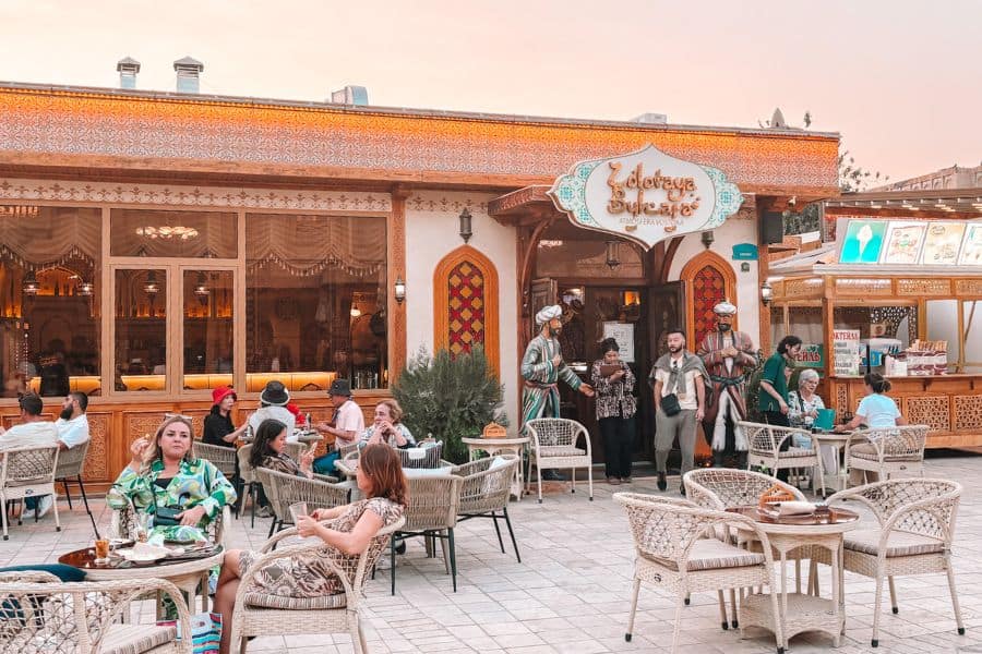 outdoor seating at zolotaya bukhara restaurant with traditional decor, wicker chairs, and diners in the historic old city