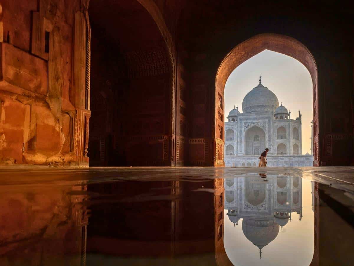 taj mahal reflected on wet marble floor framed by an arched gateway