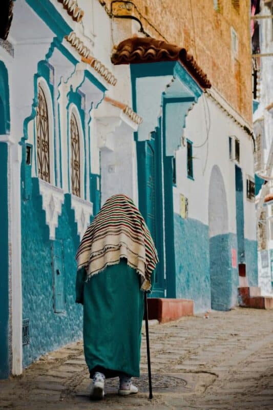 person walking through blue and white alley in chefchaouen morocco