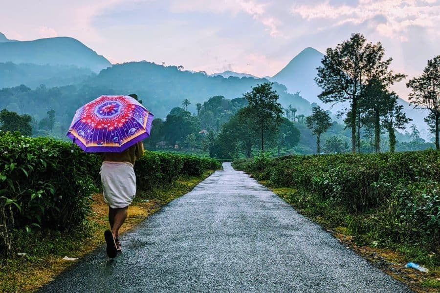 person walking with umbrella on wet road in wayanad surrounded by green mountains