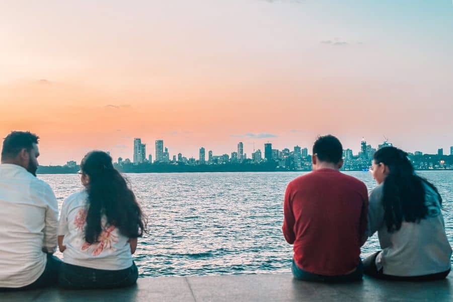 Two couples sitting on the Marine Drive promenade at sunset, watching the Mumbai skyline across the Arabian Sea