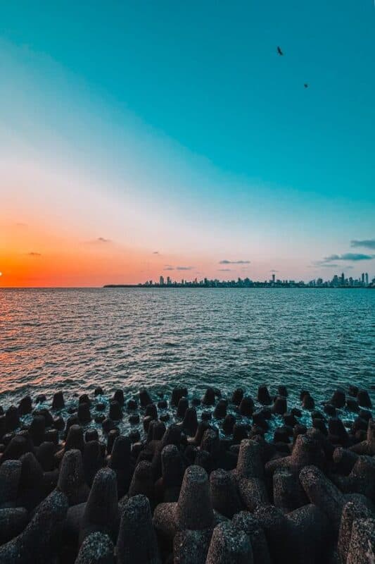 Sunset over the Arabian Sea at Marine Drive in Mumbai, with tetrapods in the foreground and the South Mumbai skyline silhouetted in the distance