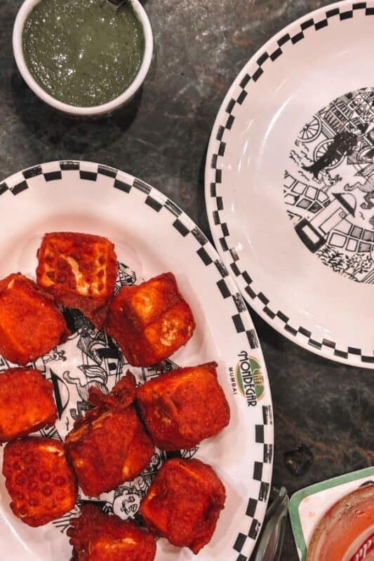 Crispy paneer koliwada on a Mario Miranda-illustrated plate at Cafe Mondegar in Colaba, with mint chutney and the cafe's iconic checkered crockery